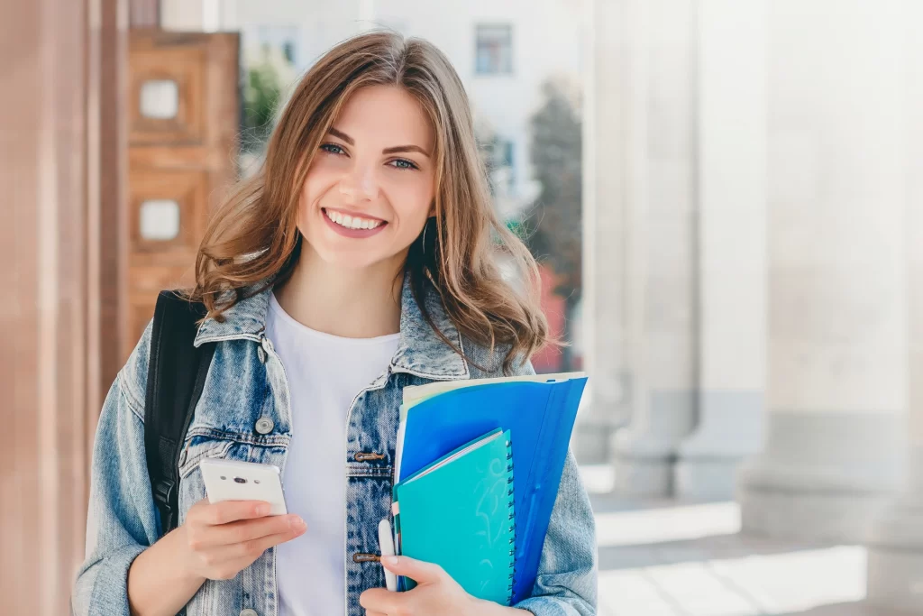 student girl smiling against university holds folders notebooks mobile phone hands